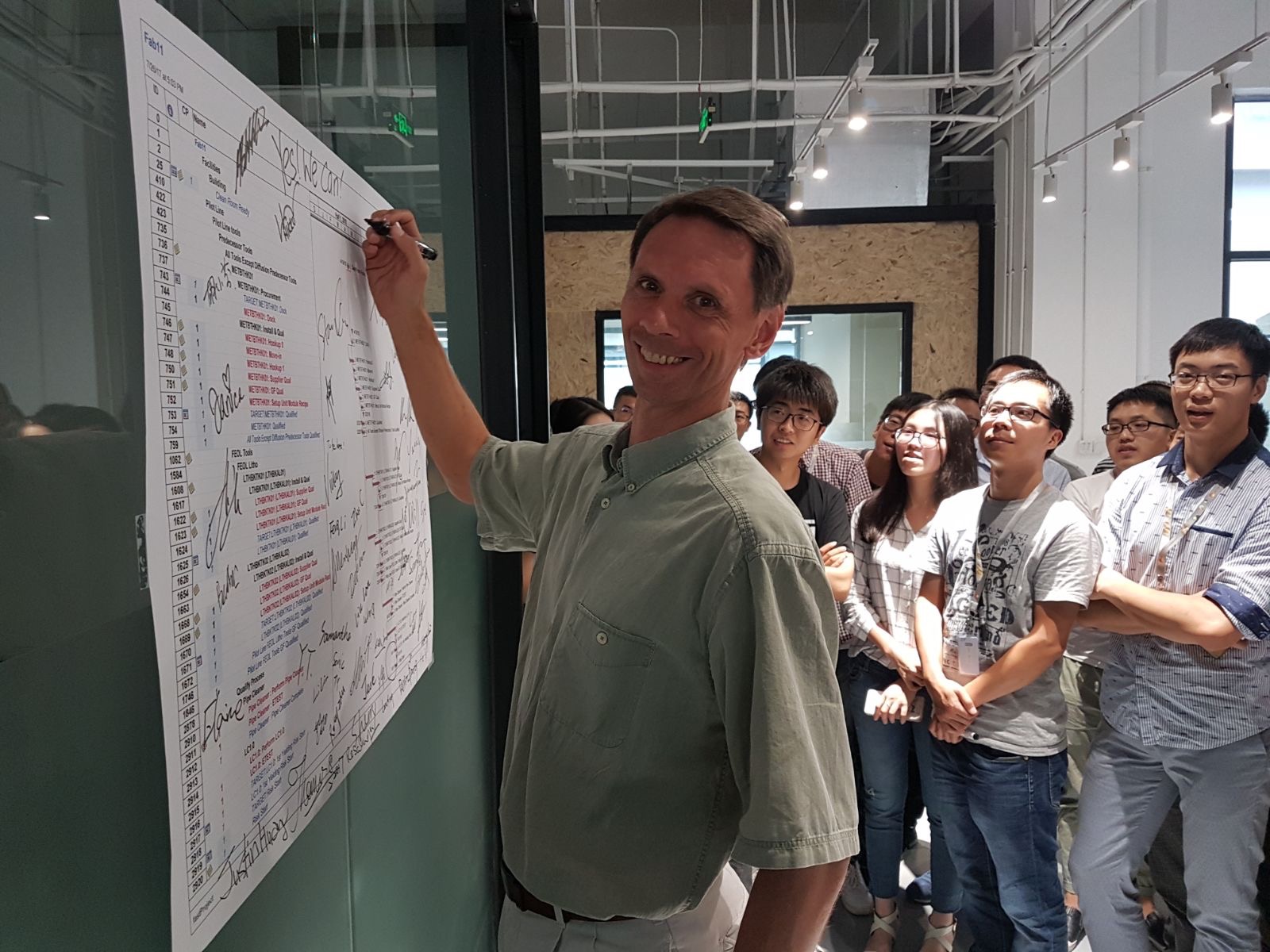 A member of the program team signing the macro plan on the wall while the rest of the team looks on